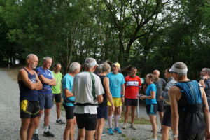 A group of people in athletic clothing stand together on a gravel path outdoors, surrounded by trees near a glorious chateau in the Loire, appearing to prepare for a run or group activity.
