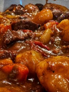 Close-up of a hearty beef stew with chunks of beef, potatoes, carrots, and red peppers in a thick, rich brown gravy.