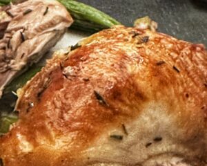 A close-up of roasted turkey with golden, crispy skin, seasoned with herbs, and green beans in the background.