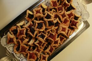 A tray filled with star-shaped cookies, some with red jam and others with dark purple jam centers, arranged neatly on a silver platter with a paper doily underneath.