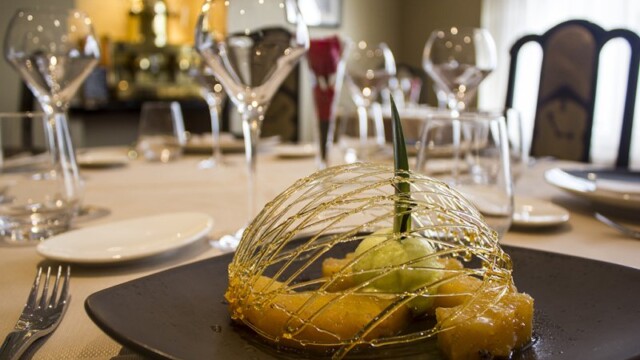 A gourmet dessert with caramelized sugar art decorates a plate with fruit pieces and a green scoop of sorbet. The table is elegantly set with wine glasses and dishes in a refined dining setting.