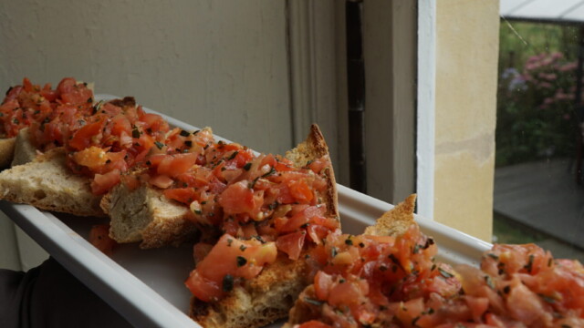 A rectangular white plate holds several pieces of toasted bread topped with diced tomatoes and herbs, held near a window overlooking the gardens of a glorious chateau in the Loire.