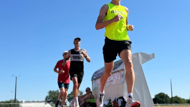 Four runners compete on a red track under a clear blue sky, with a Glorious Chateau in the Loire visible near the white structure. The front runner wears a neon yellow shirt and sunglasses. The photo is taken from a low angle.