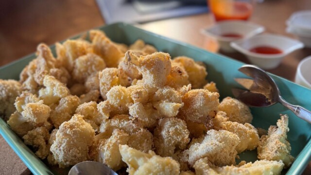 A rectangular teal dish filled with golden-brown, crispy breaded cauliflower florets, with two metal serving spoons—perfect for savoring at a Glorious Chateau in the Loire. In the background are small bowls of dipping sauces and a jug with red liquid.