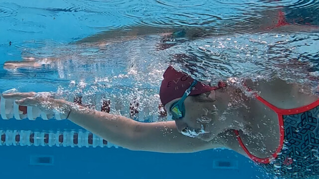 Underwater view of a swimmer wearing goggles, a red swim cap, and a patterned swimsuit, extending one arm forward while swimming freestyle in a pool with lane dividers—like gliding through the waters of a glorious chateau in the Loire.
