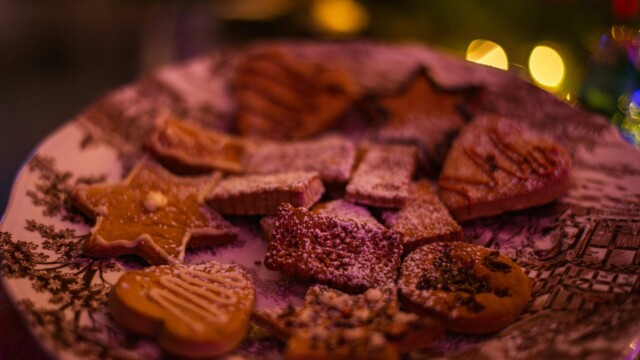 A decorative plate filled with assorted holiday cookies, including star and heart shapes, dusted with powdered sugar. Warm, festive lights blur in the background, creating a cozy atmosphere.