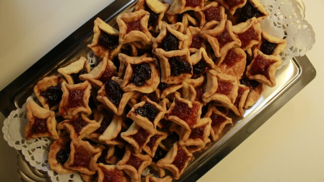 A tray filled with star-shaped cookies, some with red jam and others with dark purple jam centers, arranged neatly on a silver platter with a paper doily underneath.